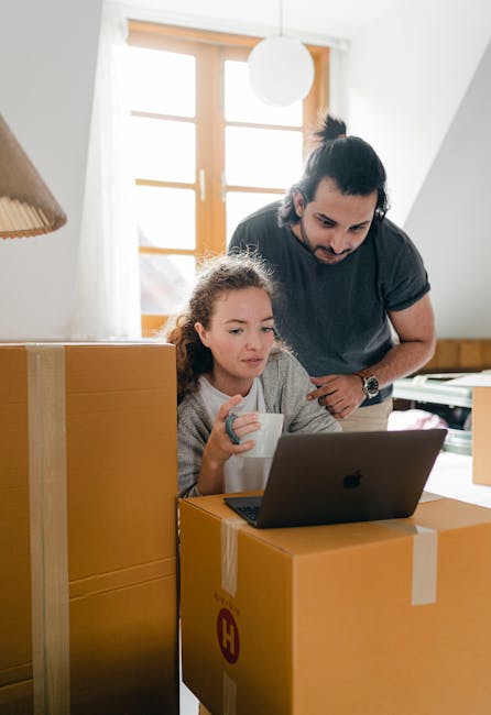 Inside a residential property during a furniture transport and home relocation process, a woman with dark hair, dressed in a white top, is seen sitting on the floor organizing packing materials. In th