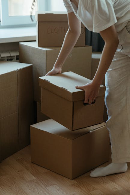 An urban street scene depicts a home relocation process with Self Storage Clapham's furniture transport and loading activities. In the foreground, two pedestrians, a woman and an older man, cross the